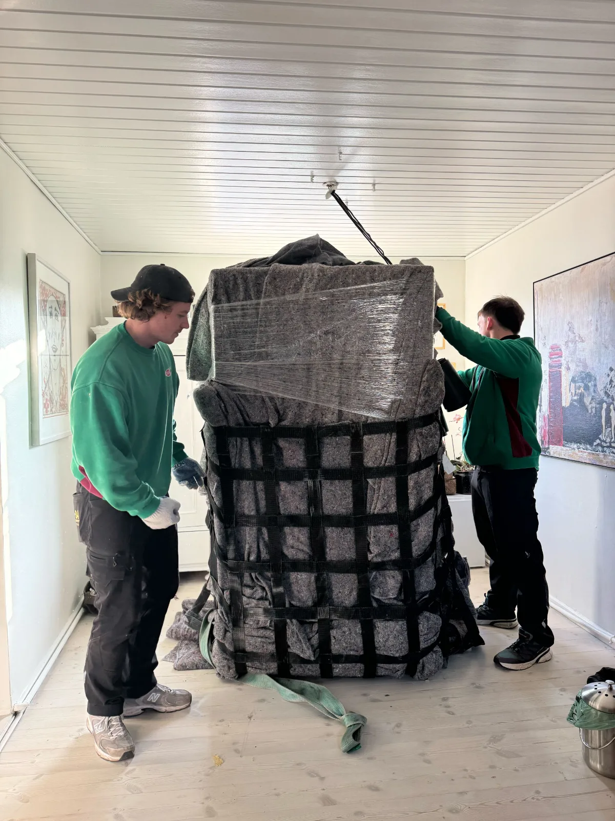 La imagen muestra a dos personas en Copenhague preparando un frigorífico americano para su traslado y protegiéndolo con mantas y film de plástico.