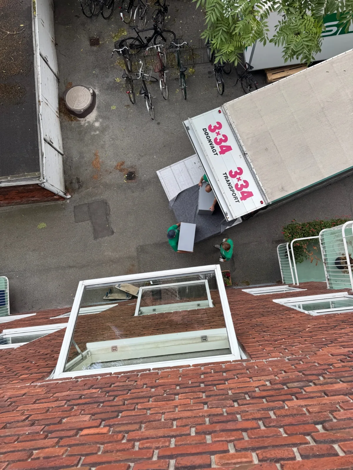 Tre flyttefolk aflæsser møbler fra en flyttevogn på en gårdsplads i København NV.