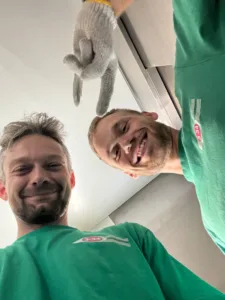 To flyttemænd i grønne T-shirts tager en selfie indendørs fra Valby til København S.