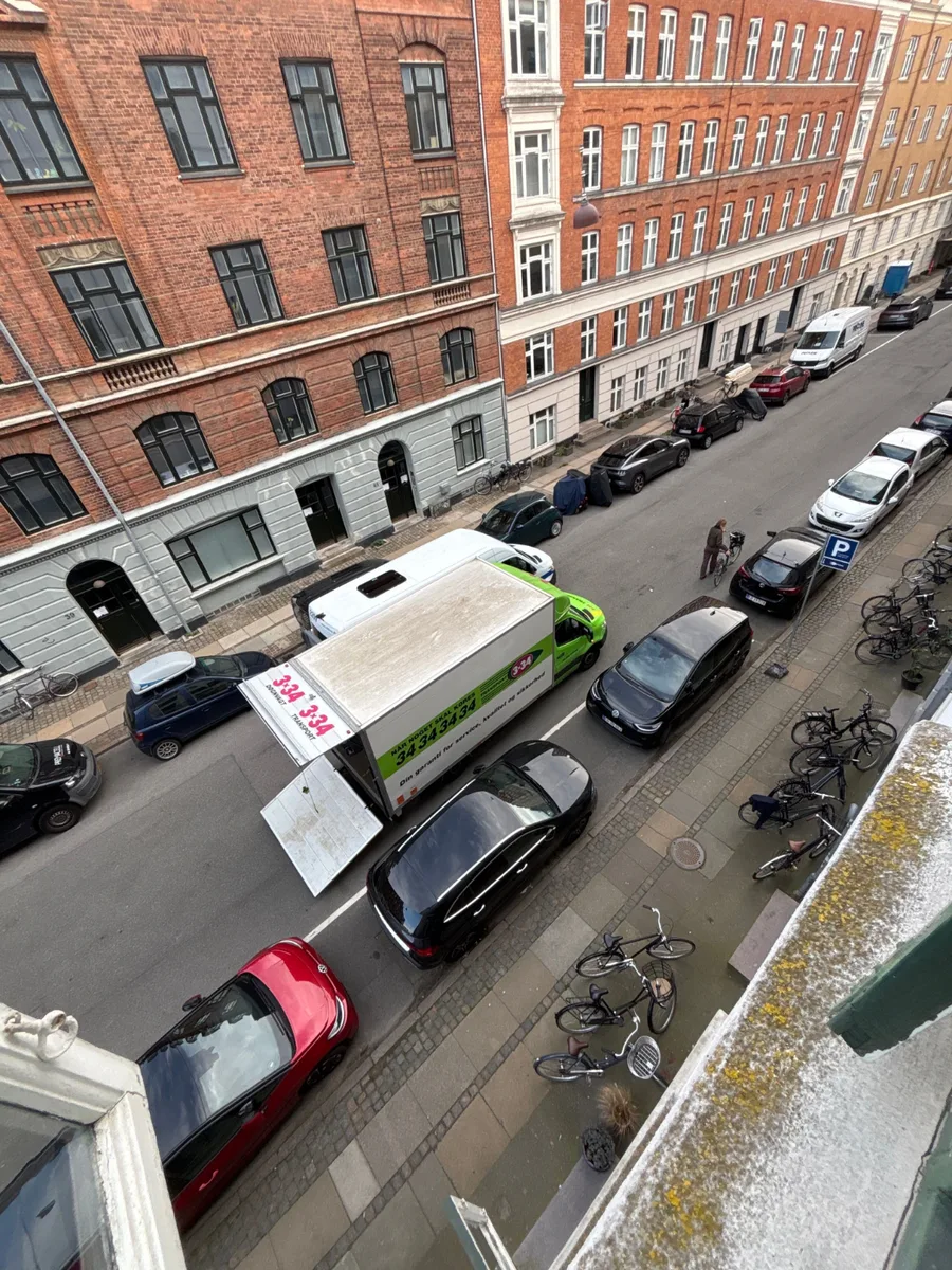 Flyttevogn parkeret i en smal gade foran en lejlighedsejendom.