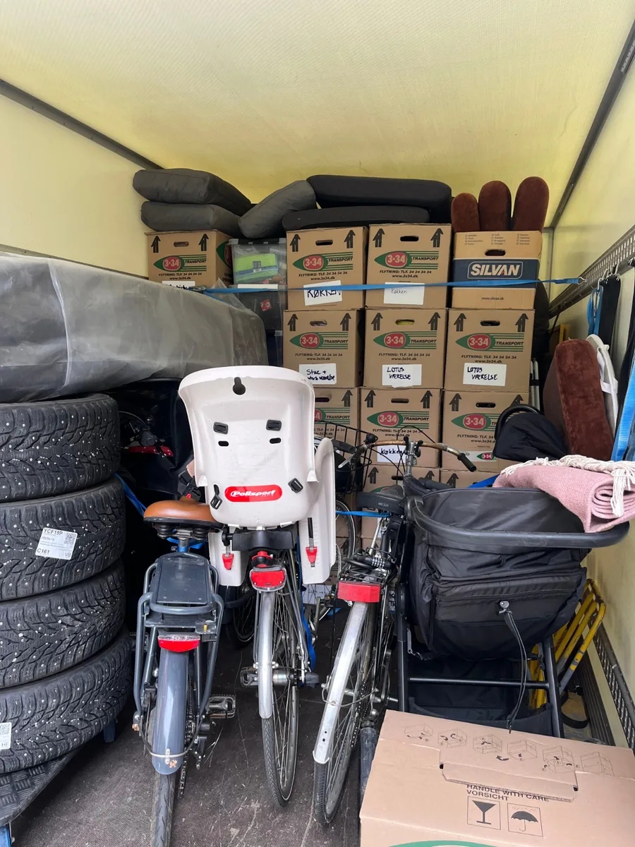 En fyldt flyttevogn med mange flyttekasser, to cykler og fire dæk.