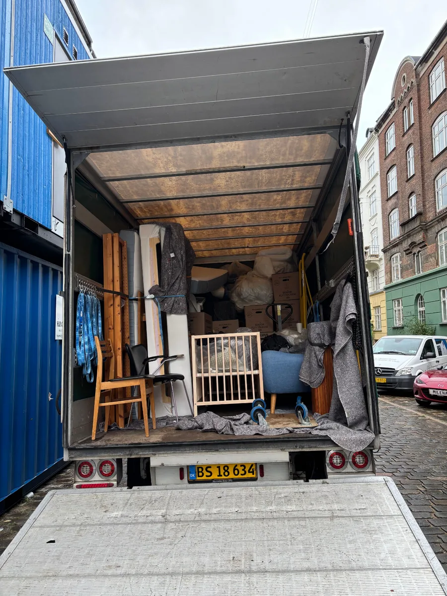 En flyttevogn er læsset med møbler og flyttekasser på en brostensbelagt gade under en flytning fra København V til København Ø.