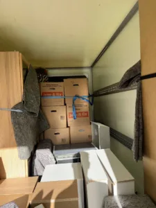En fyldt flyttevogn med flyttekasser, møbler indpakket i flyttetæpper og hvide møbeldele.