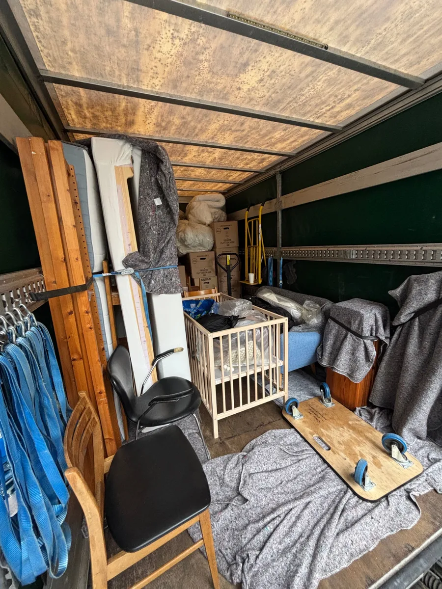 En flyttevogn er fyldt med møbler indpakket i flyttetæpper, en tremmeseng, en stol og flyttekasser.