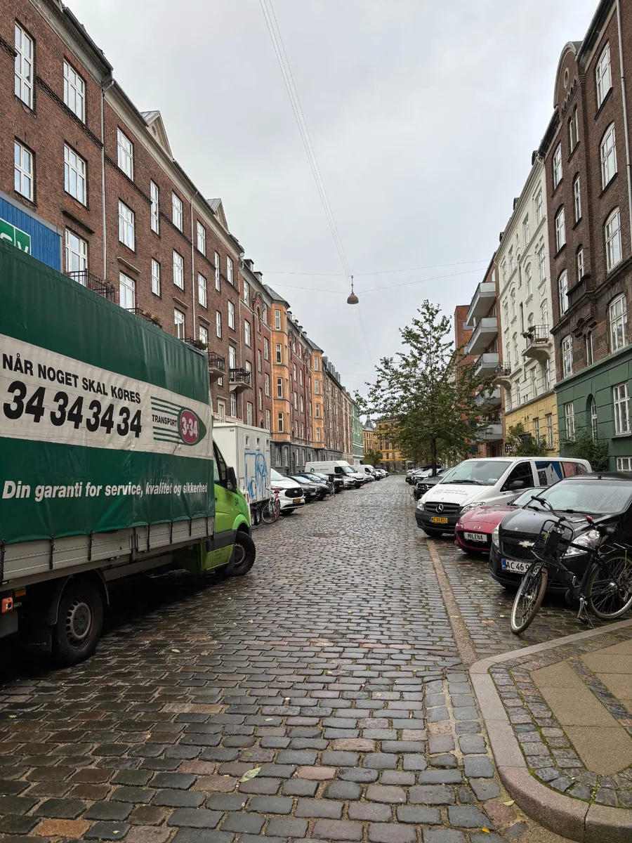 En flyttevogn er parkeret på en brostensbelagt gade mellem høje boligbygninger.