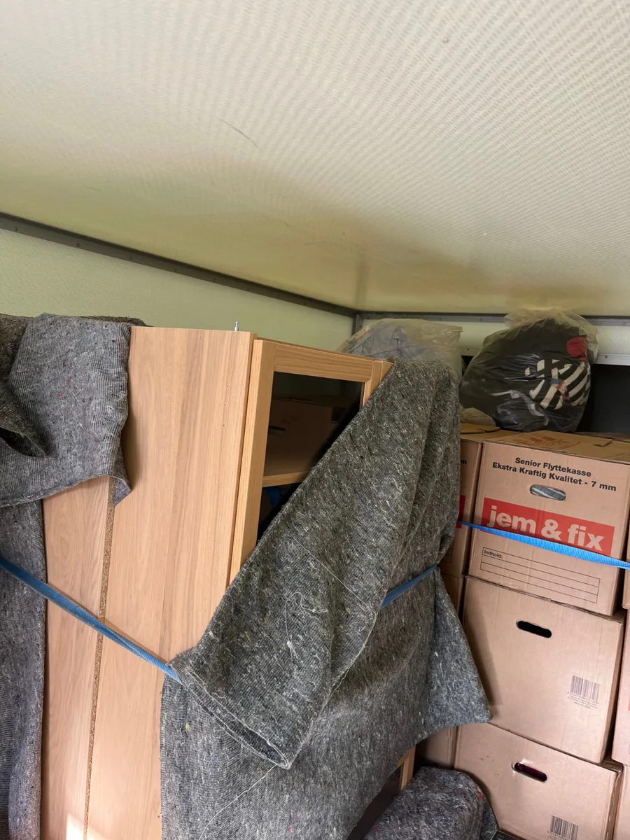 Møbler indpakket i flyttetæpper og flyttekasser står surret fast i en flyttevogn.