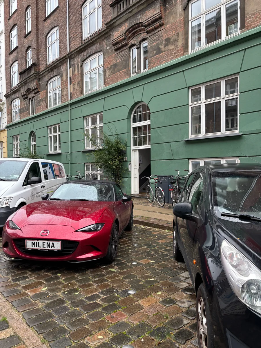 En opgang i en gård med parkerede biler på vådt brosten.