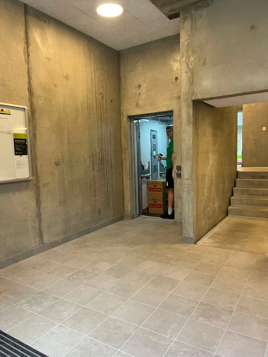 To papkasser står i en åben elevator i en rå betonopgang.