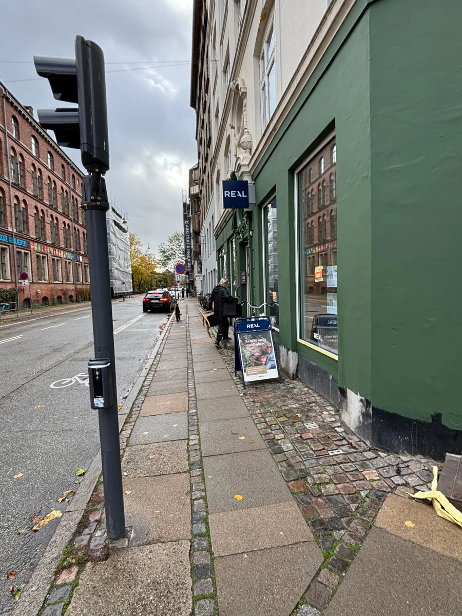 En person står ved en butik på et fortov langs en gade.