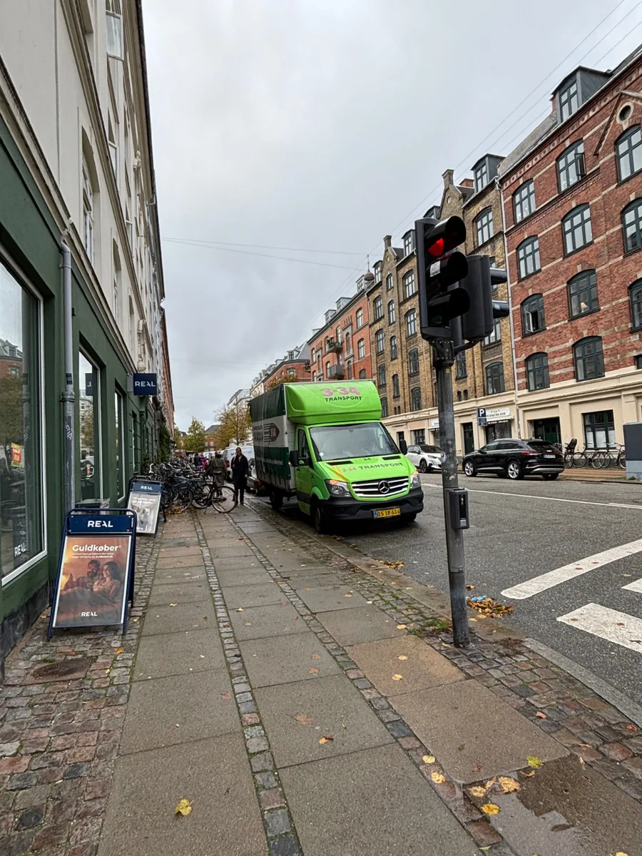 En grøn transportvogn holder parkeret ved fortovet på en bygade.